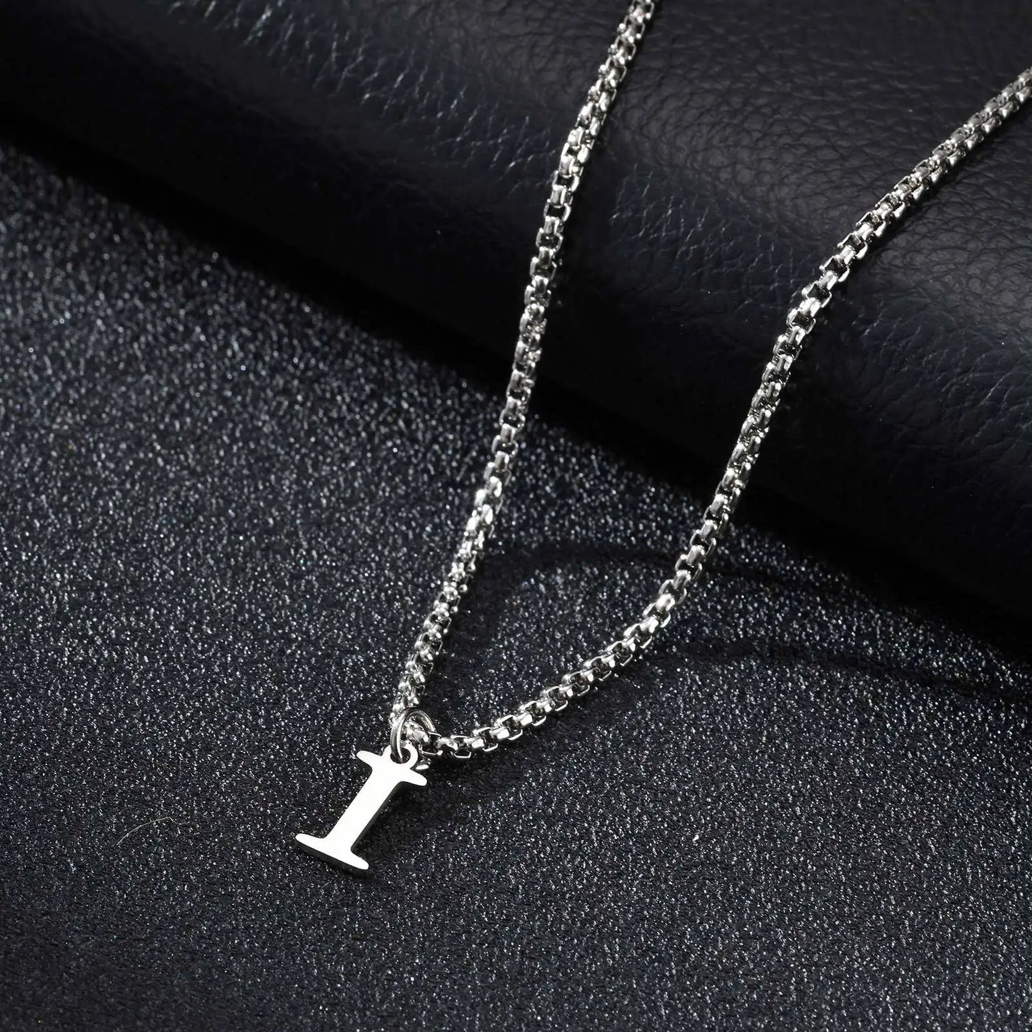 Silver necklace with a 'I' pendant on a black textured surface