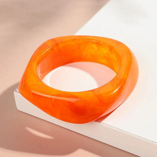 Orange bangle on a white surface with a beige background