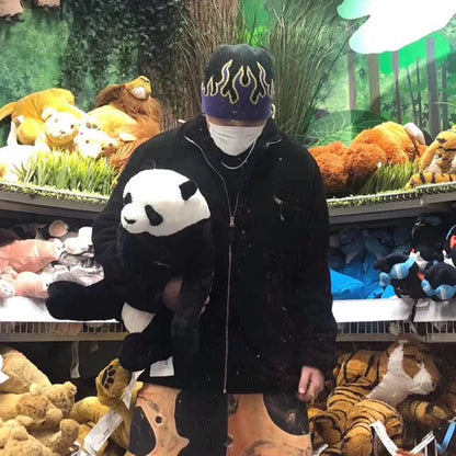 Person holding a panda plush toy in a toy store with stuffed animals and greenery in the background.