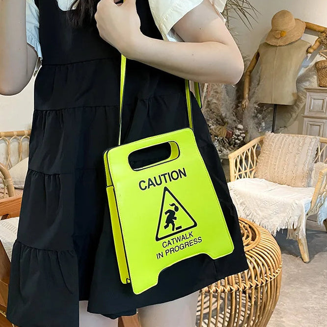 Person holding a bright yellow 'Caution: Catwalk in Progress' sign in an indoor setting.