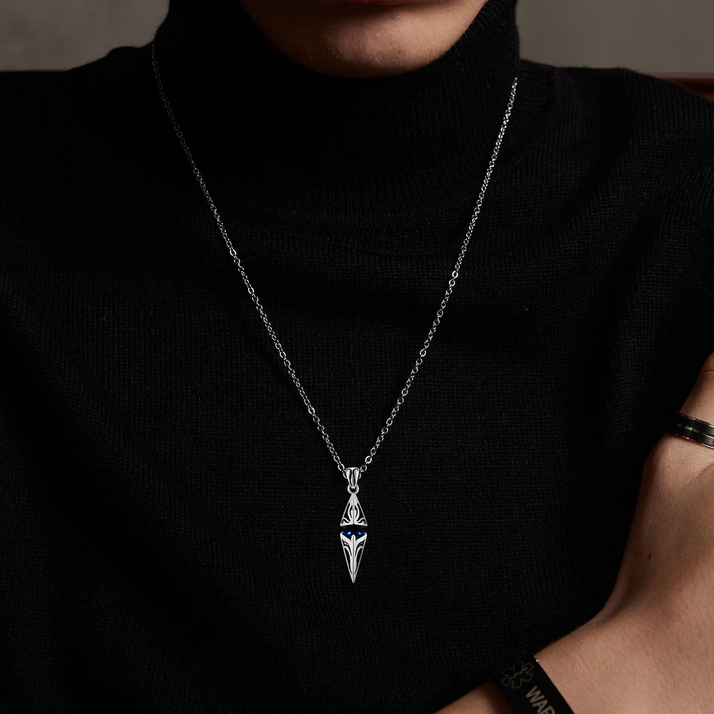 Person wearing a black turtleneck with a silver necklace featuring a unique pendant.