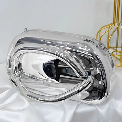 Silver handbag on a white surface with a gold decorative item in the background