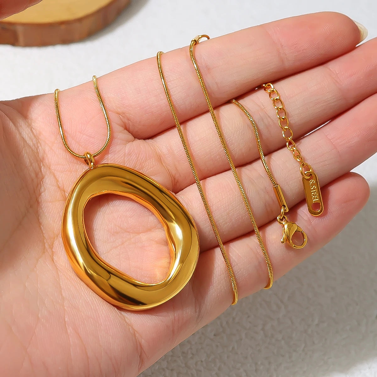 Gold necklace with a large pendant held in a hand against a neutral background