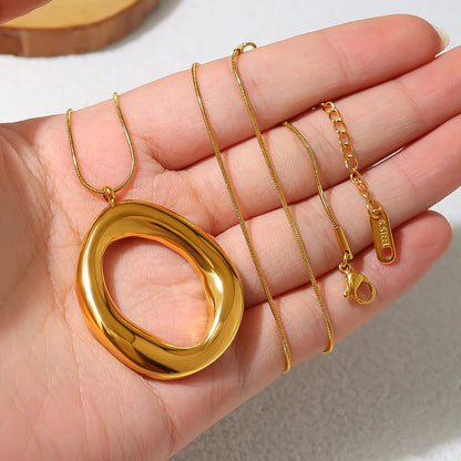 Gold necklace with a large pendant held in a hand against a neutral background
