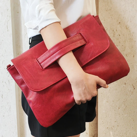 Red leather clutch held by a person against a neutral background