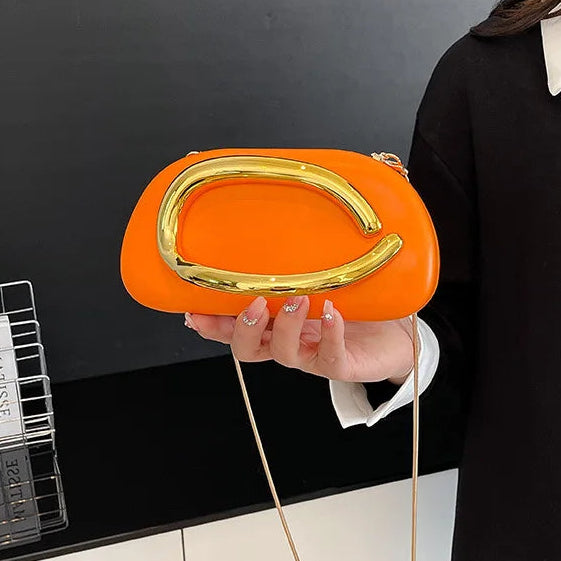 Person holding an orange clutch bag with a gold handle against a black background