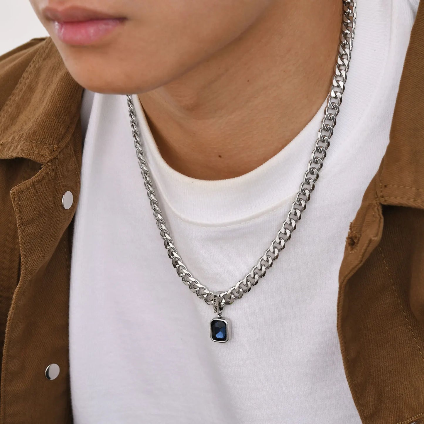 Person wearing a silver chain necklace with a pendant, brown jacket, and white shirt.