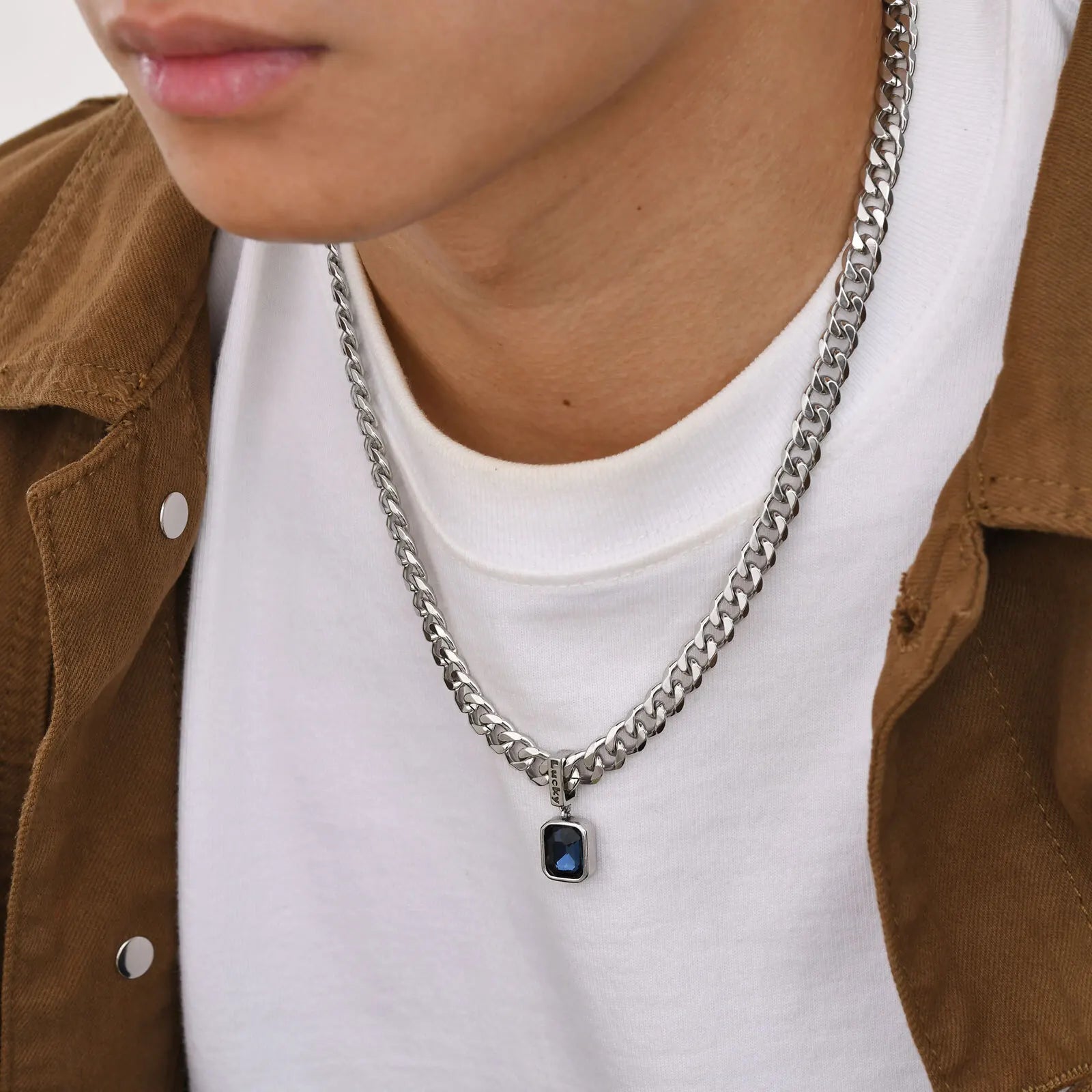 Person wearing a silver chain necklace with a pendant, brown jacket, and white shirt.