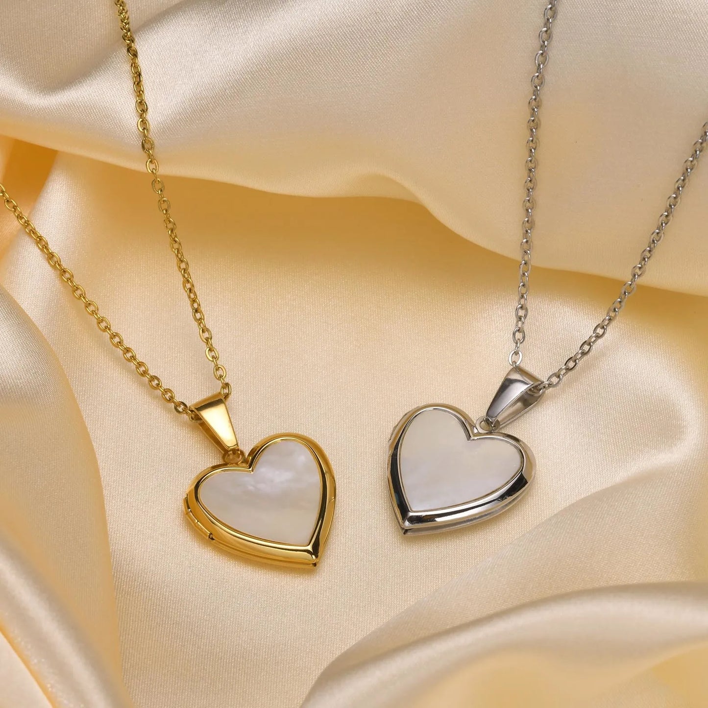 Two heart-shaped pendants, one gold and one silver, on a satin surface.