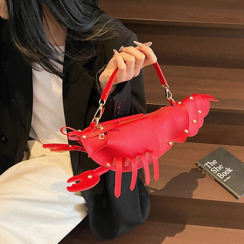 Person holding a red lobster-shaped handbag with a book titled 'The She Book' in the background.