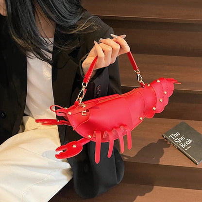 Person holding a red lobster-shaped handbag with a book titled 'The She Book' in the background.