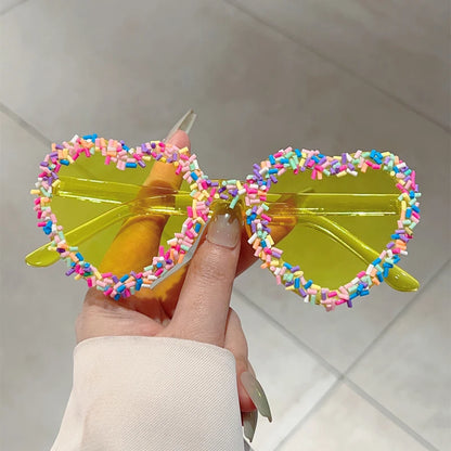 Sunglasses with colourful sprinkles held by a hand against a neutral background