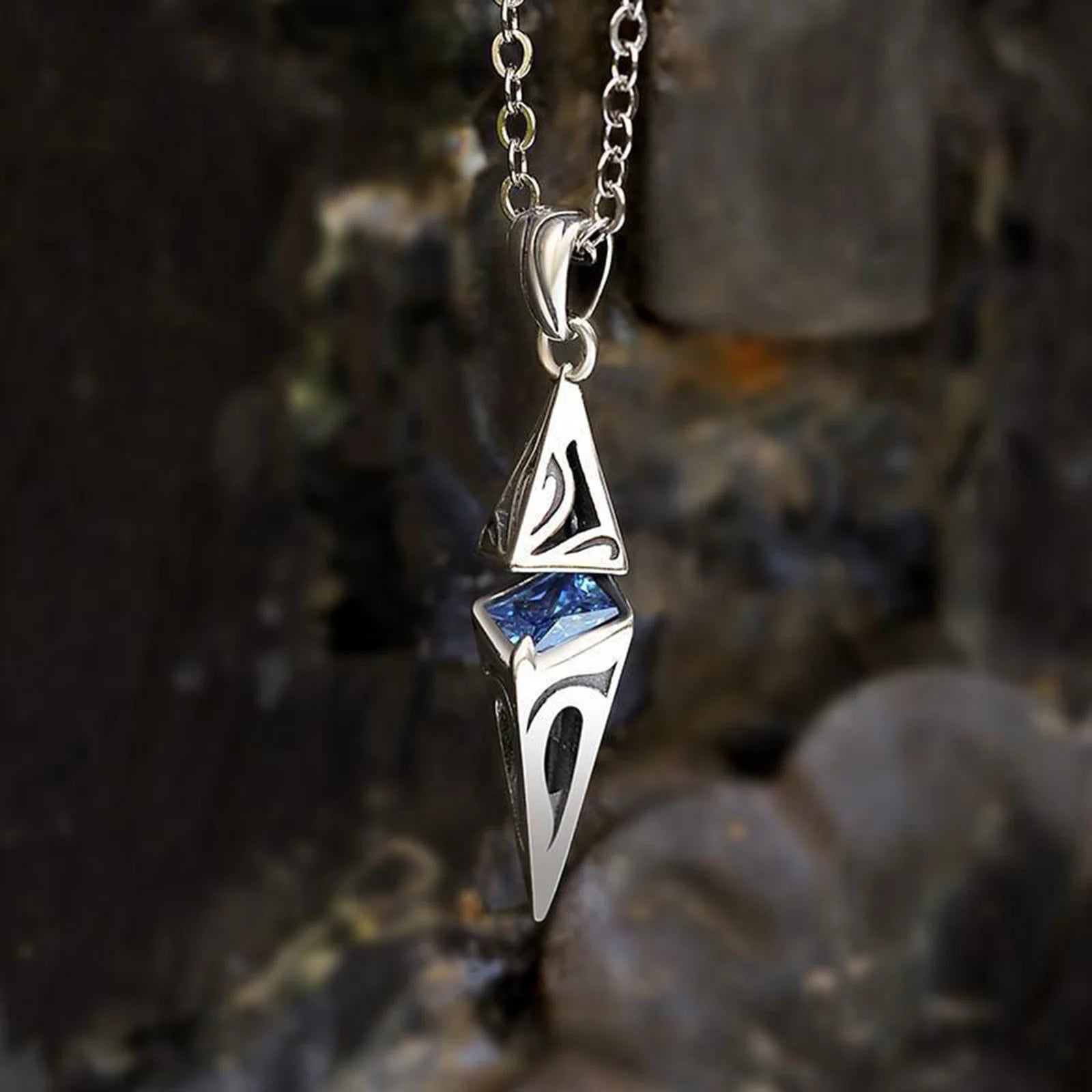 Silver pendant with blue gemstone on a chain against a rocky background