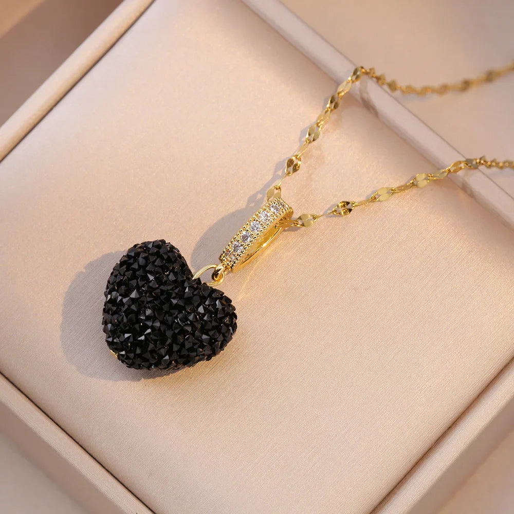 Gold necklace with a black heart-shaped pendant on a beige surface