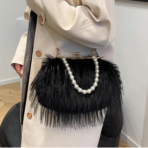 Person holding a black handbag with feather details and pearl accents.