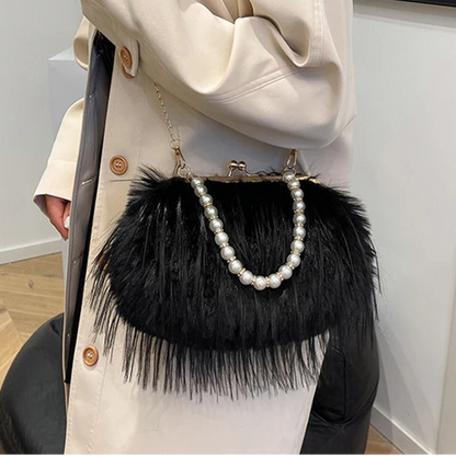 Person holding a black handbag with feather details and pearl accents.