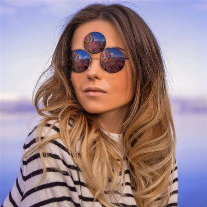 Woman wearing round sunglasses with a scenic reflection, against a blue sky background