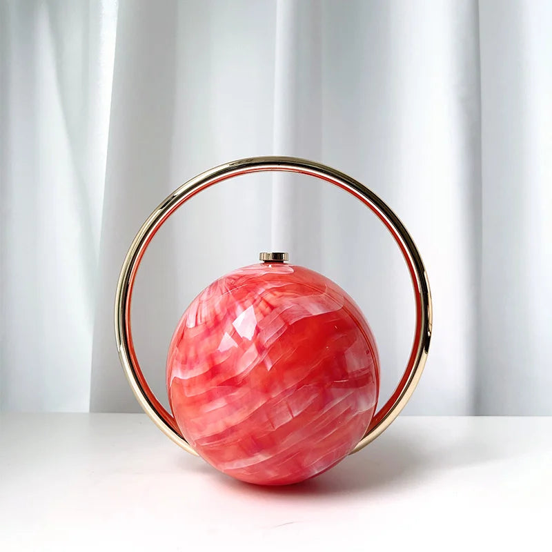 Decorative clutch bag with a pink marbled sphere and gold circular frame on a white background