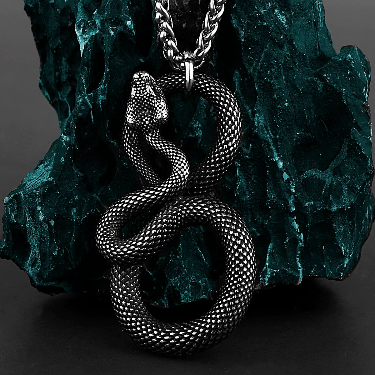 Silver snake pendant necklace on a textured green stone background