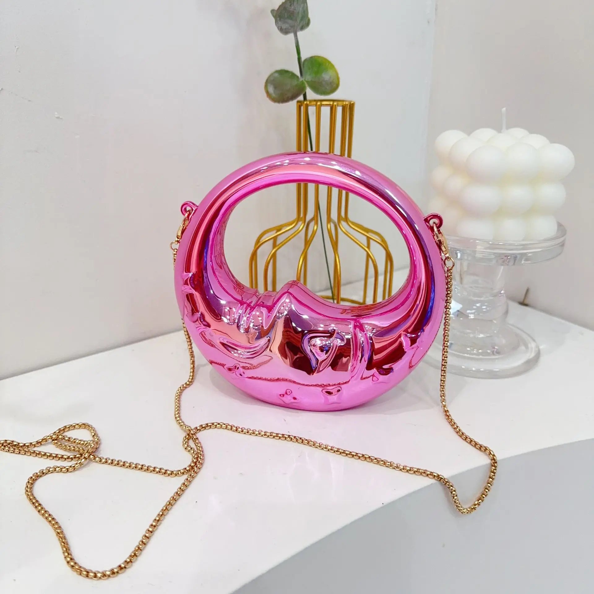 Pink crescent handbag with gold chain on a white surface