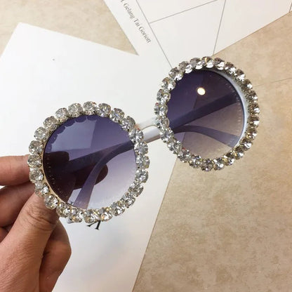 Sunglasses with decorative frame held by a hand on a textured surface