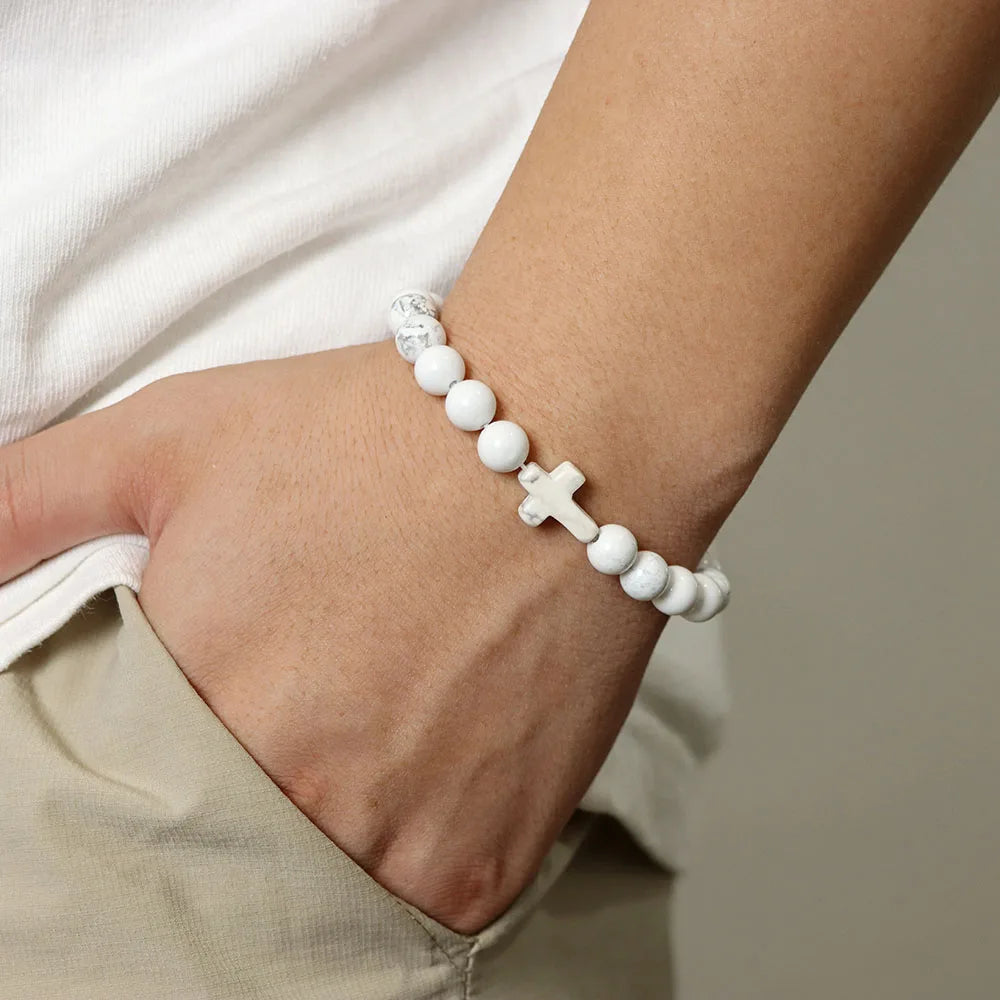 White beaded bracelet with cross charm on wrist against a neutral background