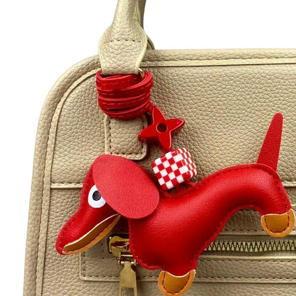 Red dachshund-shaped purse charm attached to a beige handbag.