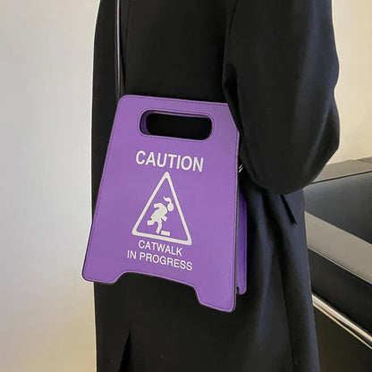 Person holding a purple bag with 'Caution: Catwalk in Progress' text and symbol.