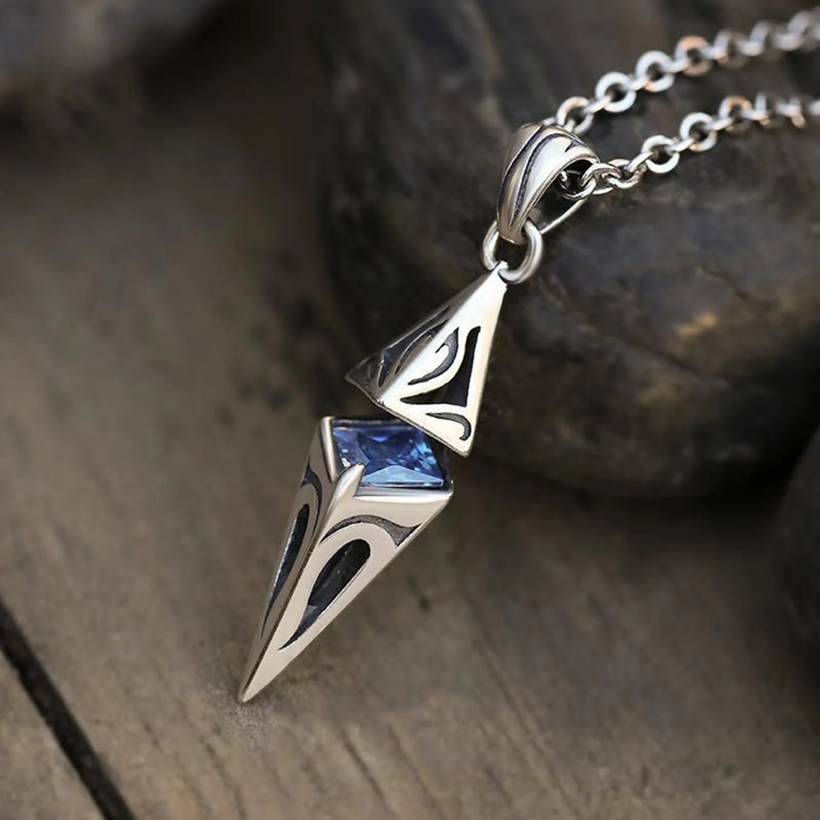 Silver pendant with blue gemstone on a chain, placed on a wooden surface.