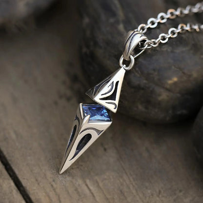 Silver pendant with blue gemstone on a chain, placed on a wooden surface.