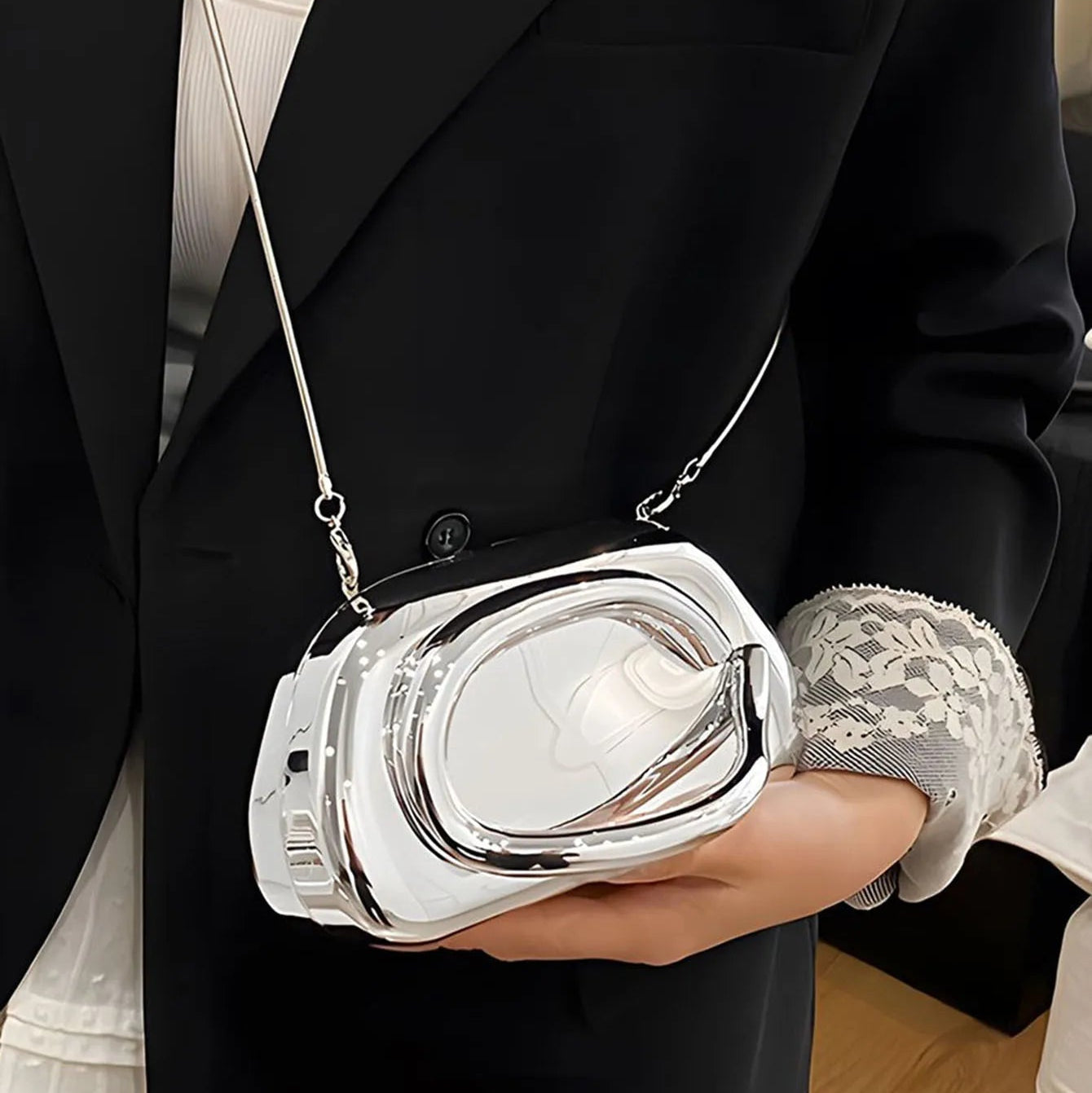 Person holding a silver handbag with a unique design, wearing a black blazer.