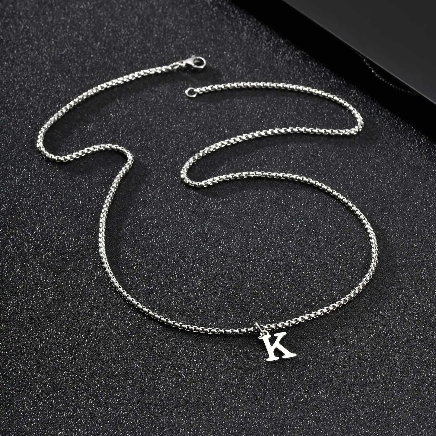 Silver chain necklace with a 'K' pendant on a black background