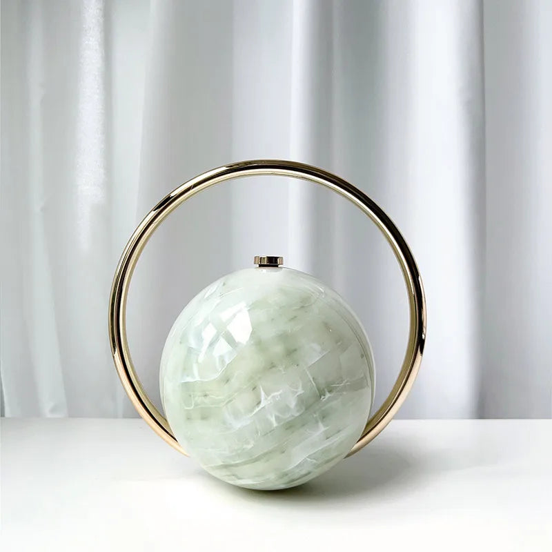 Clutch bag with a green spherical center and gold circular frame on a white surface.