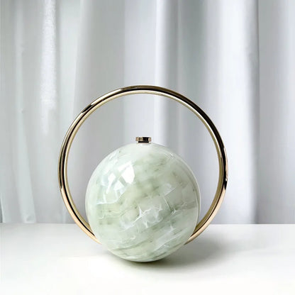 Decorative clutch bag with a green spherical center and gold circular frame on a white surface.