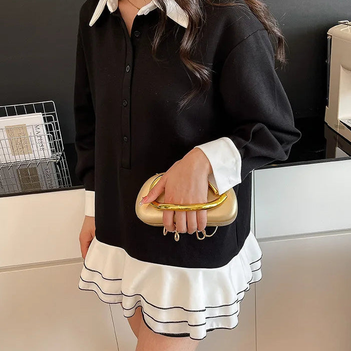 Person wearing a black shirt with white trim and a white skirt, holding a gold clutch.