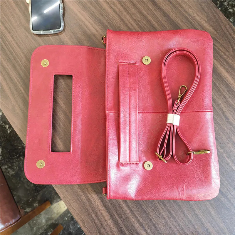 Red leather clutch bag with a strap on a wooden surface