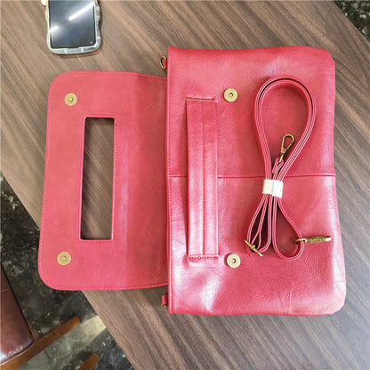 Red leather clutch bag with a strap on a wooden surface