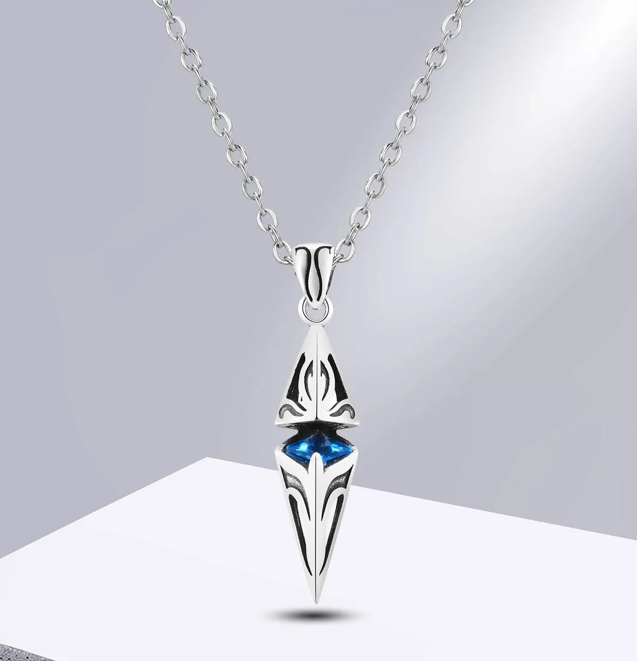 Silver pendant necklace with blue gemstone on a grey background.