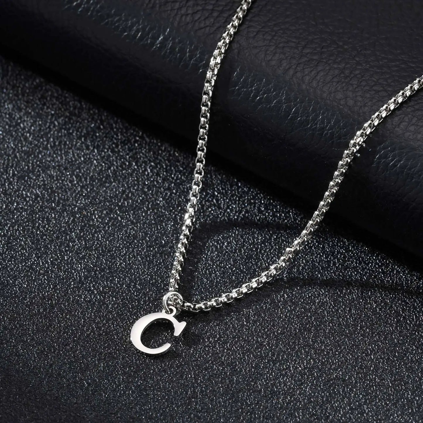 Silver necklace with a 'C' pendant on a black textured surface