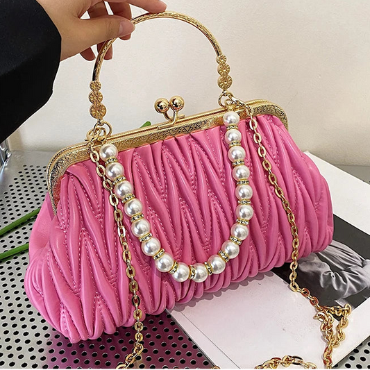 Pink handbag with pearl details held by a hand on a white background
