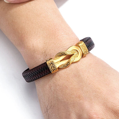 Gold bracelet with a brown cord on a wrist against a white background