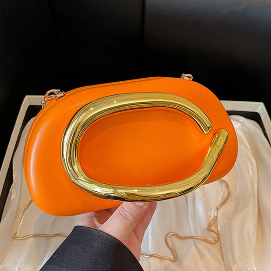 Orange handbag with gold handle held by a person, displayed on a black couch.