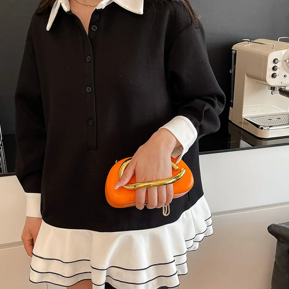 Person wearing a black and white outfit holding an orange clutch in a kitchen setting.