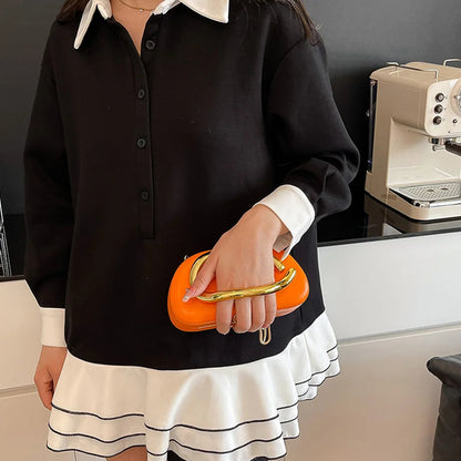 Person wearing a black and white outfit holding an orange clutch in a kitchen setting.