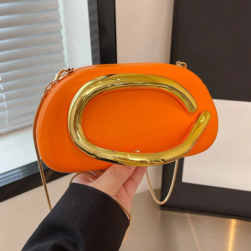 Orange clutch bag with gold handle held by a person indoors.