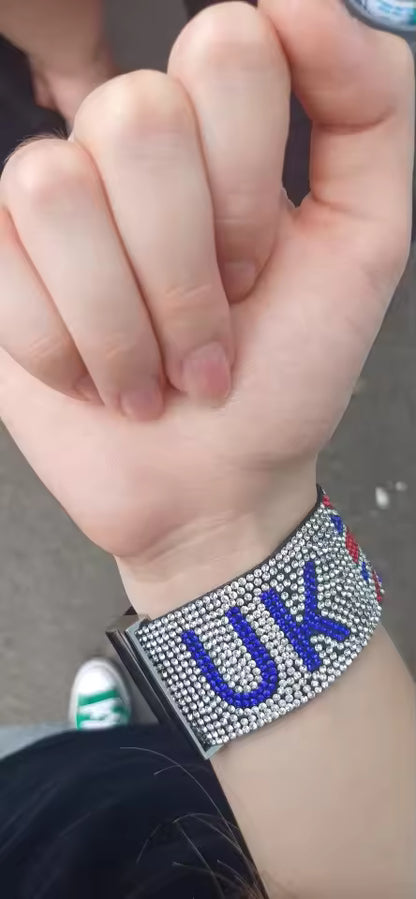 Hand wearing a bracelet with 'UK' letters on a blurred background