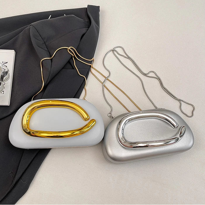 Two handbags, one gold and one silver, on a light surface with a dark fabric background.